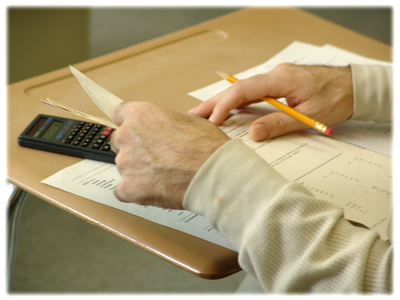 image of inmate's hands on school desk, holding pencil and calculator